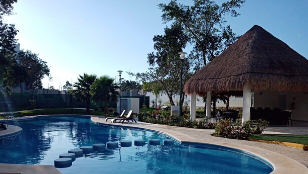 A swimming pool with lounge chairs, a thatched-roof structure, and surrounding greenery.
