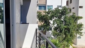 A modern apartment with a balcony, large windows, and a view of neighboring buildings and greenery.