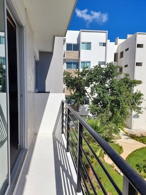 A modern apartment with a balcony, large windows, and a view of neighboring buildings and greenery.
