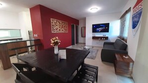 A modern living room with a dark wooden dining table, a sofa, and a TV mounted on the wall.