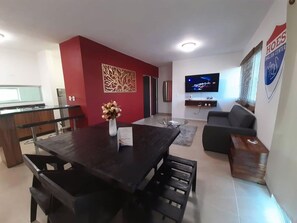 A modern living room with a dark wooden dining table, a sofa, and a TV mounted on the wall.