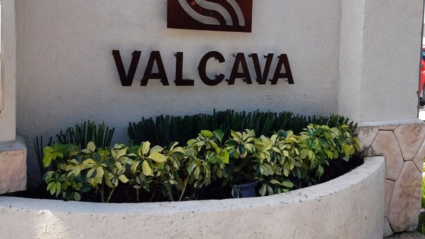 A sign with the name "VALCAVA" and a logo, surrounded by a landscaped area with plants.
