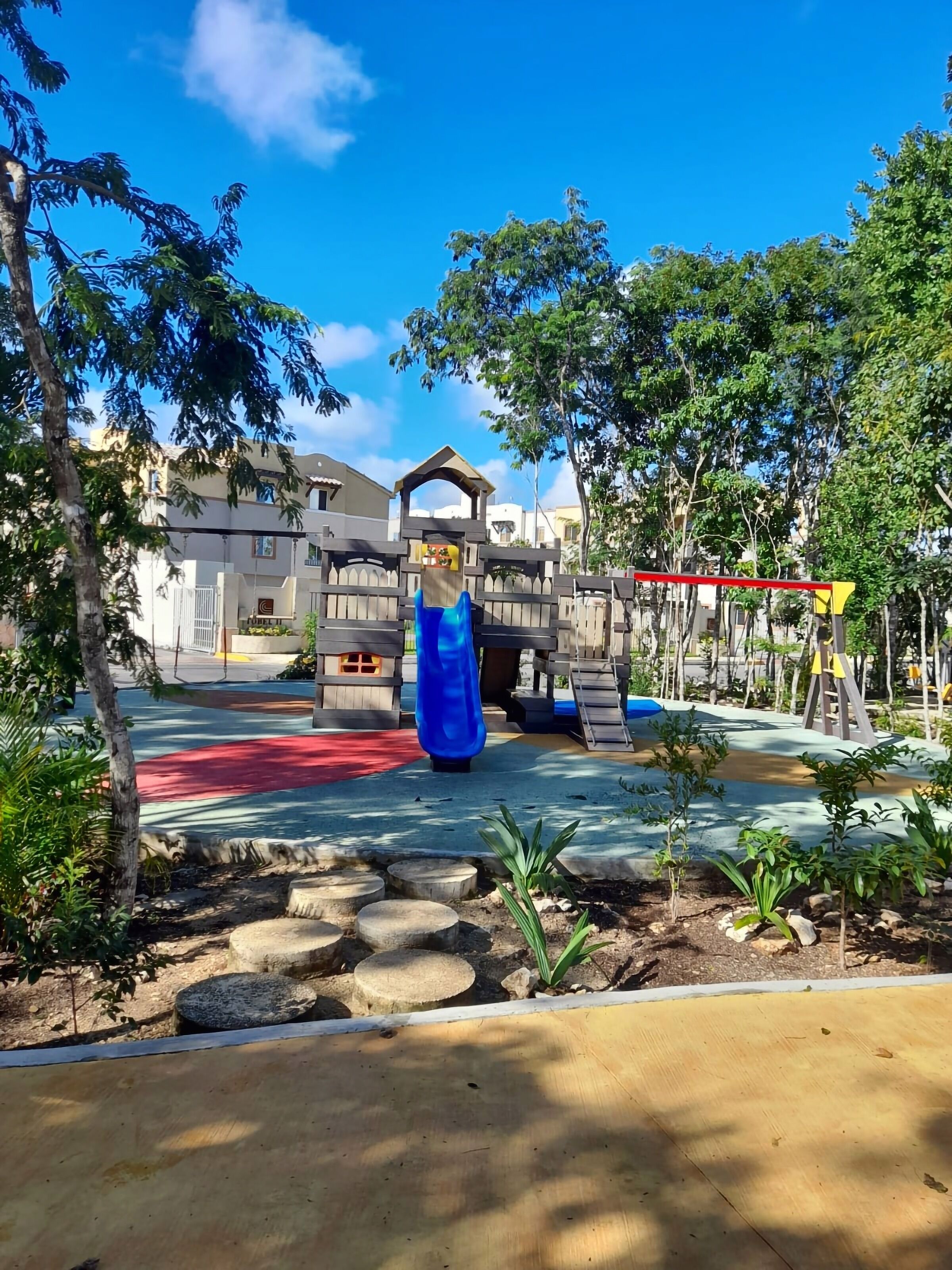 Ein Spielplatz mit einer blauen Rutsche, einer gelb-roten Spielanlage und einem hölzernen Zaun.