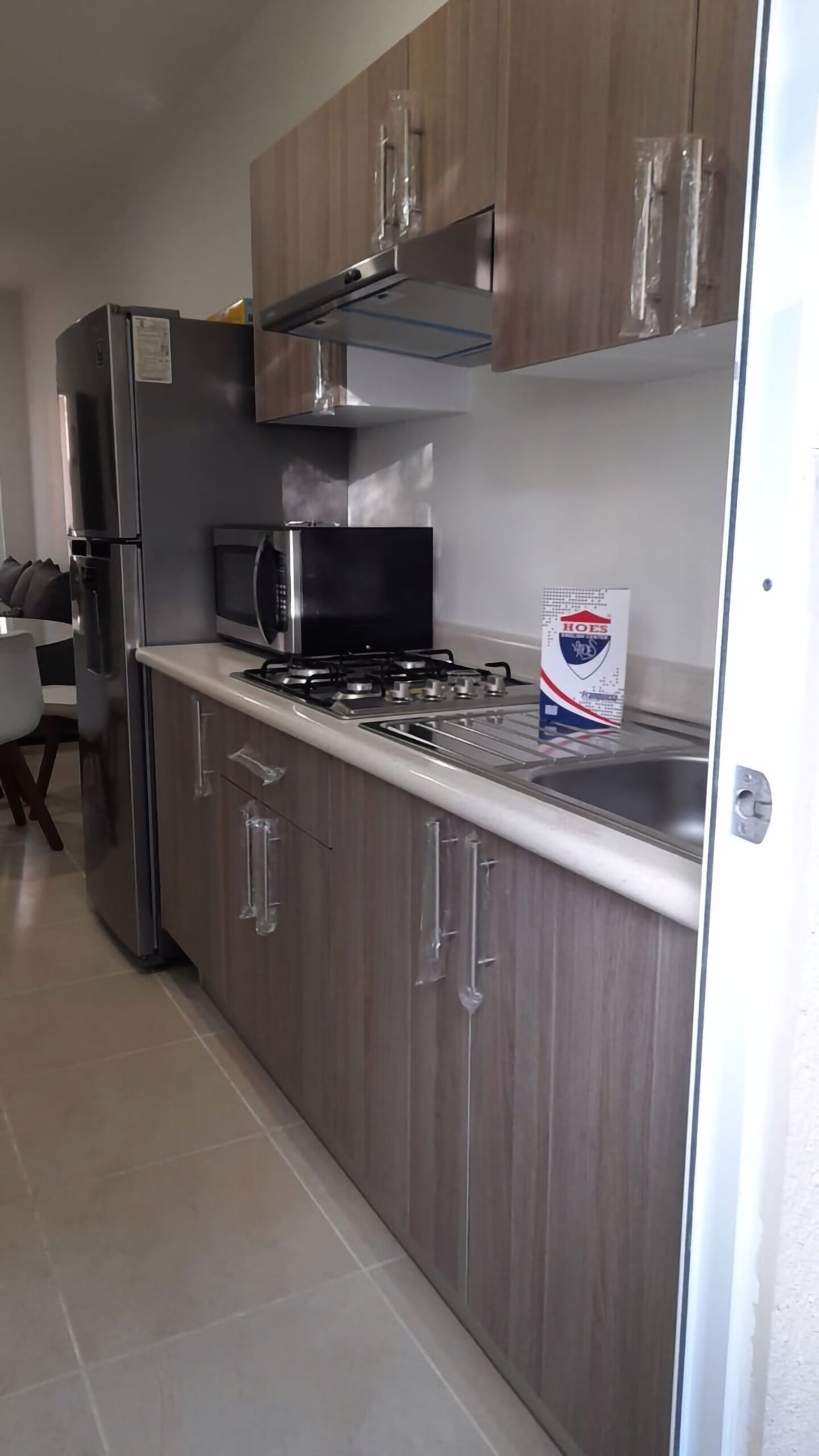 A modern kitchen with a stainless steel refrigerator, microwave, gas stove, and wooden cabinets.
