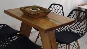 Een eetruimte met een houten tafel, zwarte netstoelen, een gevlochten mand met een plant en een ronde spiegel aan de muur.