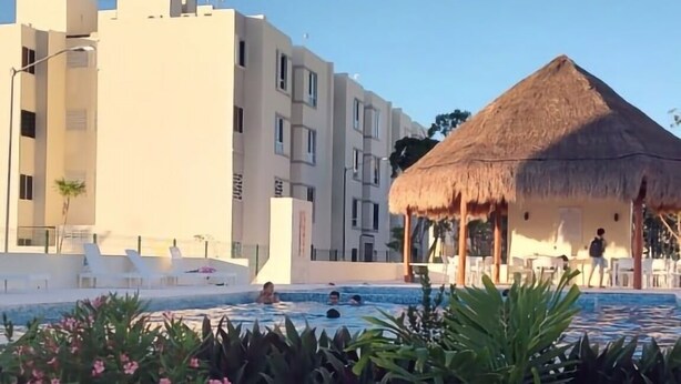Een hotel met een zwembad, een gebouw met rieten dak en moderne gebouwen op de achtergrond.