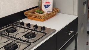 Een keuken met zwarte kastjes, een gasfornuis, een magnetron en een decoratieve vaas met gedroogde bloemen.