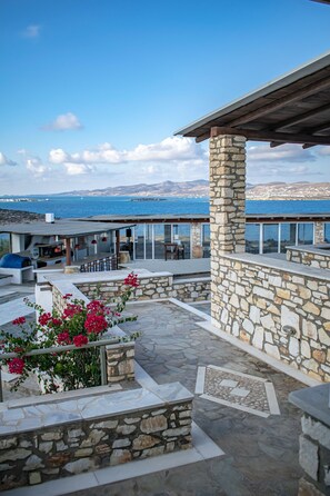 A stone patio with a view of the sea, outdoor seating, and a barbecue area.