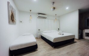 Una habitación de hotel con dos camas, un ventilador de techo, un equipo de aire acondicionado y piso de madera.