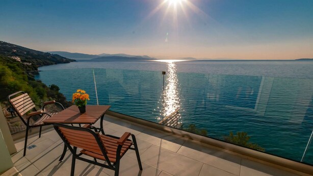 A balcony with a table and chairs overlooking a body of water with a sunset reflection. - "room in Guest Room - Room With Private Pool" (Corfu)