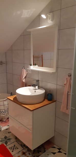 Een moderne badkamer met een witte wastafel, een rond wasbakje, een spiegel en een klein plankje met een plantje.