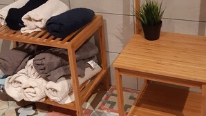 Une pièce avec une table en bois, une étagère où sont pliées des couvertures et une plante en pot.