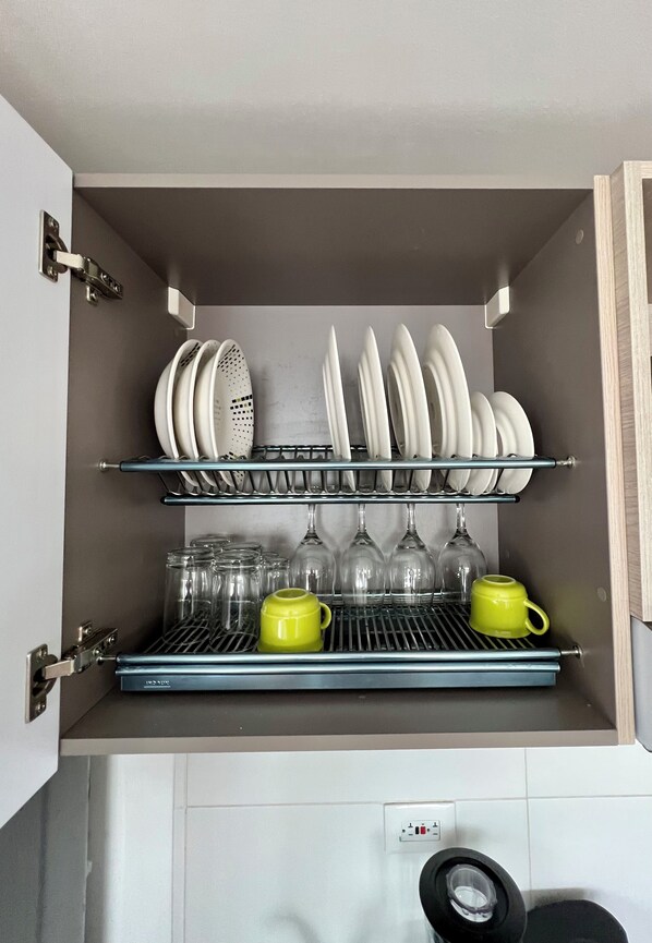 Un meuble de cuisine avec des étagères où sont rangées des assiettes, des verres et une tasse jaune.