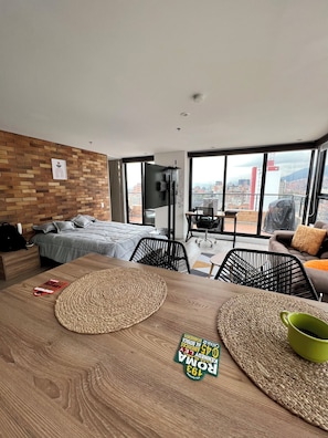 A modern hotel room with a large bed, a dining table, a TV, and a city view.