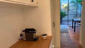 Une cuisine équipée d’un plan de travail, d’une machine à café, d’un saladier et d’une fenêtre donnant sur des palmiers.