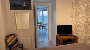 Hotellihuone, jossa on sänky, televisio, tuoli, pöytä tuoleineen, merinäköala ja taulu seinällä.