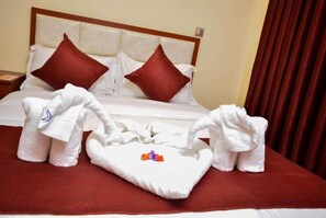 Una cama bien tendida con almohadas rojas, una colcha blanca y dos toallas blancas con diseño floral.
