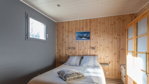 A bedroom with a wooden paneled wall, a bed with a fluffy pillow, a nightstand, and a window.