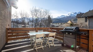 A wooden deck with a table and chairs, a grill, and a view of mountains.