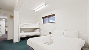 A hotel room with a bunk bed, a single bed, a window with blinds, a lamp, and a view of the outside. - Alpine Heights 11B - Mt Hotham (Hotham Heights)