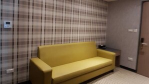 Une pièce avec un canapé jaune, un papier peint à carreaux, un tapis rayé et une porte.