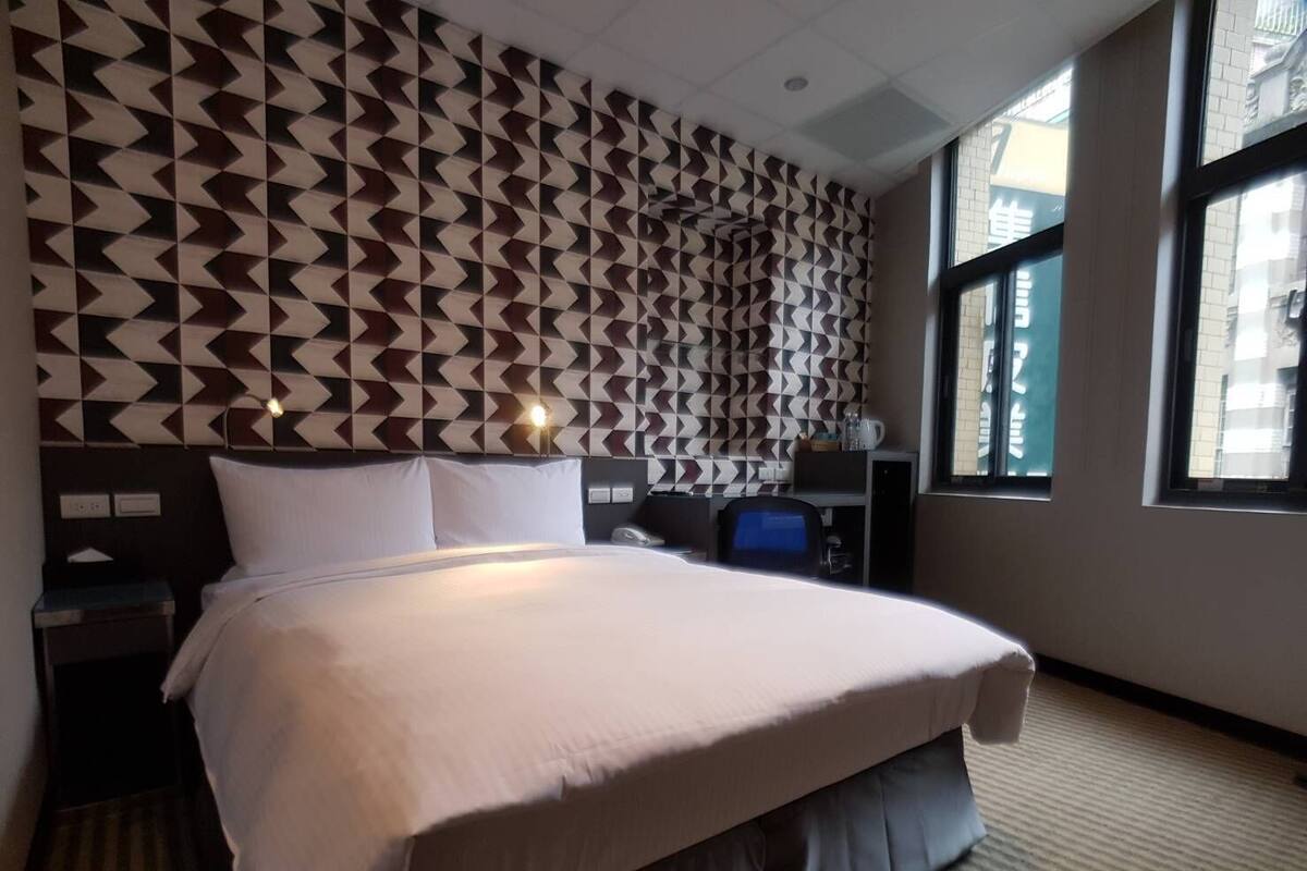 Una habitació d'hotel amb un llit, un escriptori, una cadira i una finestra.