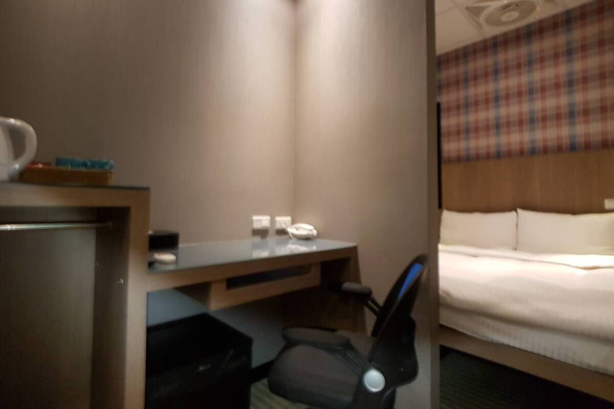 Habitació d'hotel amb un llit, una taula de nit amb telèfon, una cadira i una taula petita amb una tassa i mocadors.