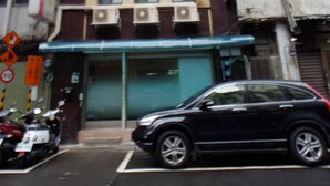 Un bâtiment à la façade moderne, une voiture garée et une moto devant.