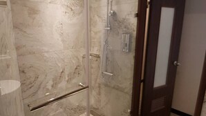 Une salle de bain avec une douche en verre, des toilettes et des murs en marbre.