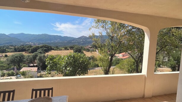Ein überdachter Außenbereich mit Tisch und Stühlen, Blick auf die Landschaft und ein Bergpanorama in der Ferne.