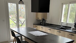 Eine moderne Küche mit einer großen Kücheninsel, Holzschränken und einer schwarzen Arbeitsplatte. Es gibt drei Barhocker und eine Hängeleuchte.
