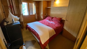 Une chambre dans une cabane en bois, avec un lit, une commode et une fenêtre avec des rideaux.