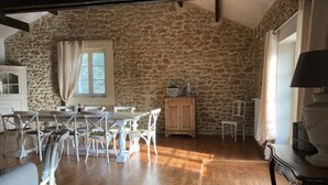 A dining area with a stone wall, wooden table, white chairs, and a cabinet. - Today's comfort in yesterday's mas in the heart of Provence (Suze la Rousse)