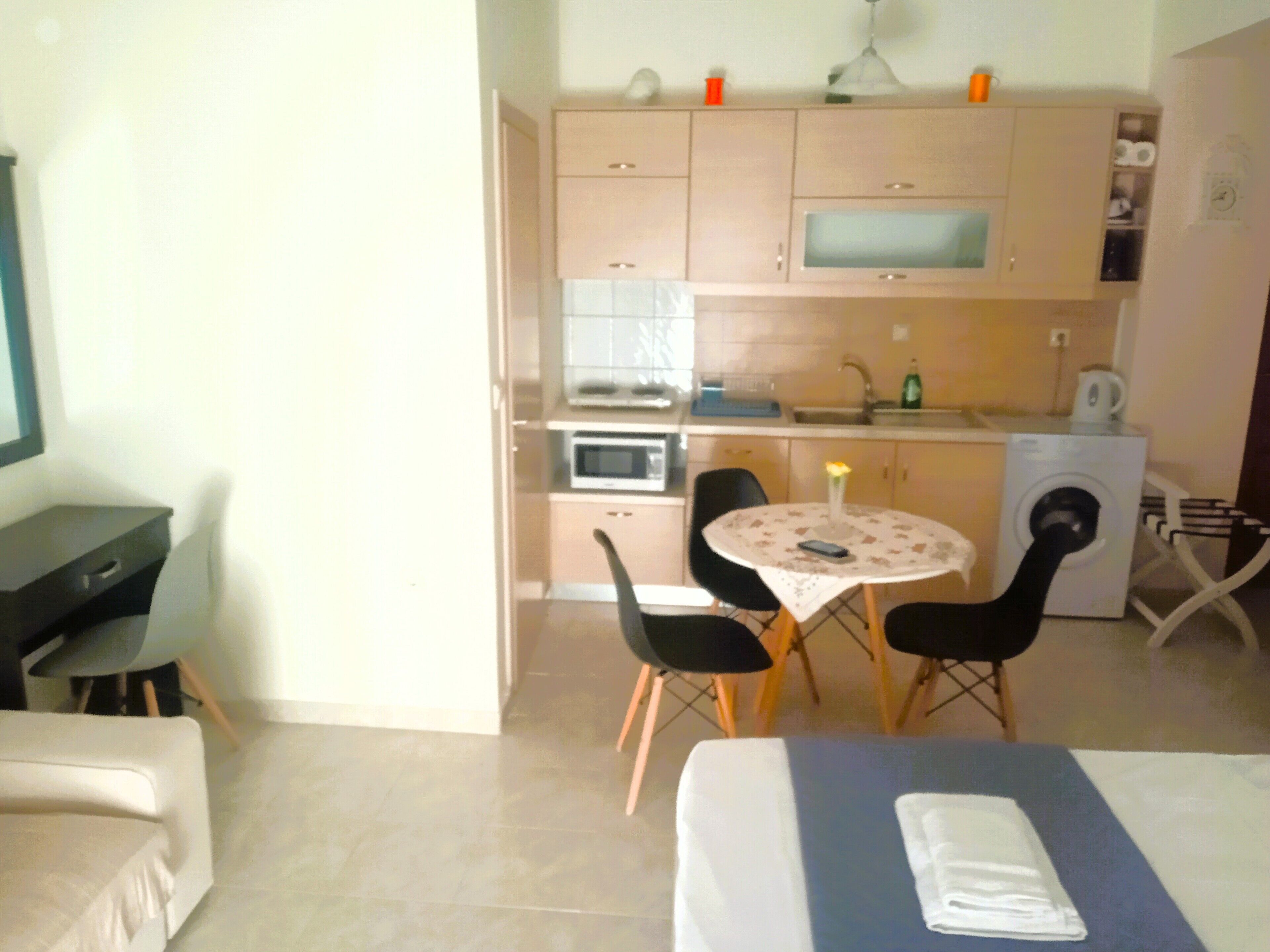 A compact living space with a kitchenette, a dining area with a table and chairs, and a bed with a neatly folded towel.