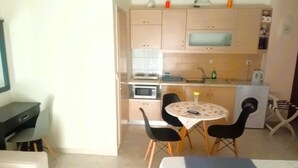 A compact living space with a kitchenette, a dining area with a table and chairs, and a bed with a neatly folded towel. - Alkioni City Apartments (Chania)