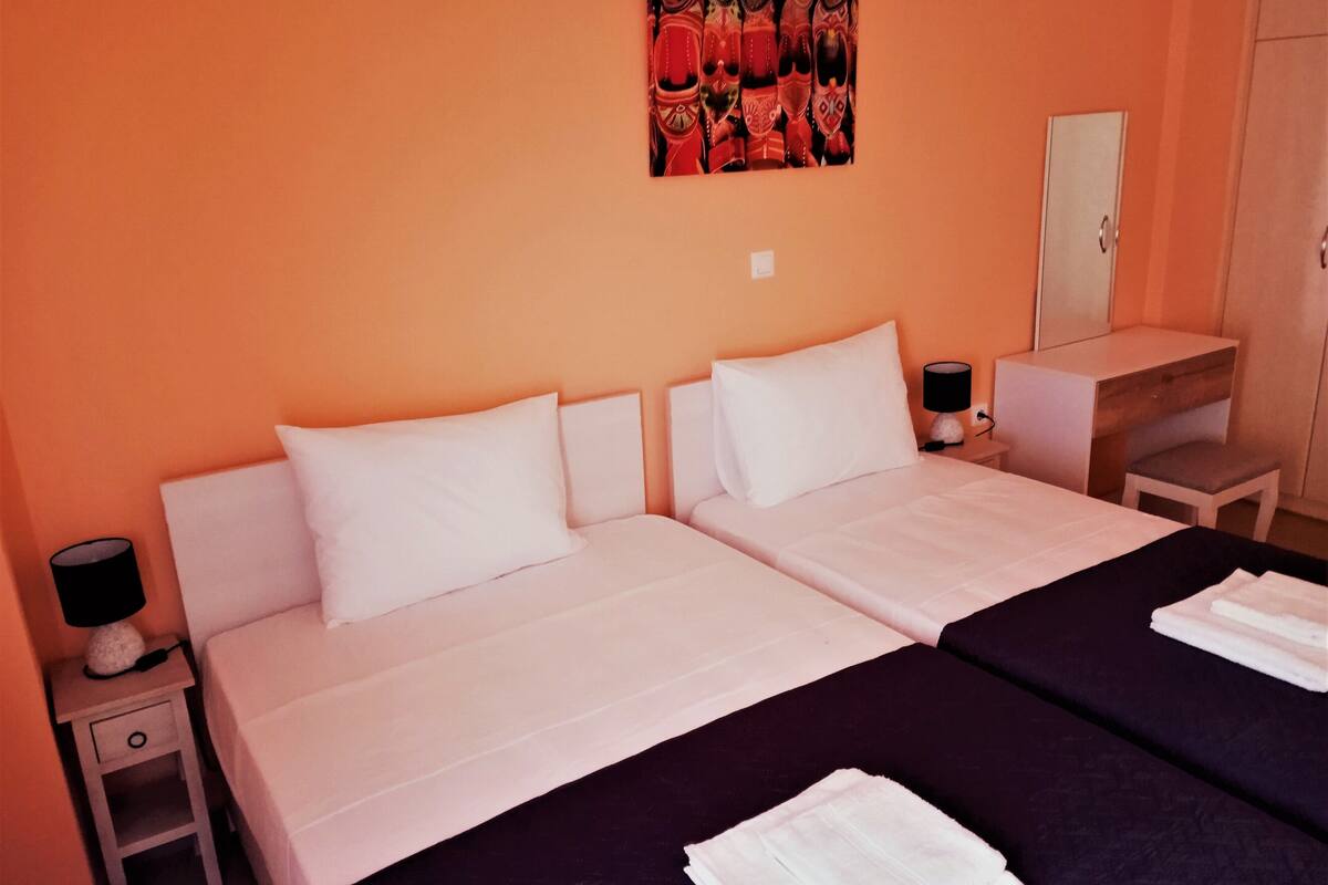 A hotel room with two beds, a desk, a chair, and a lamp.