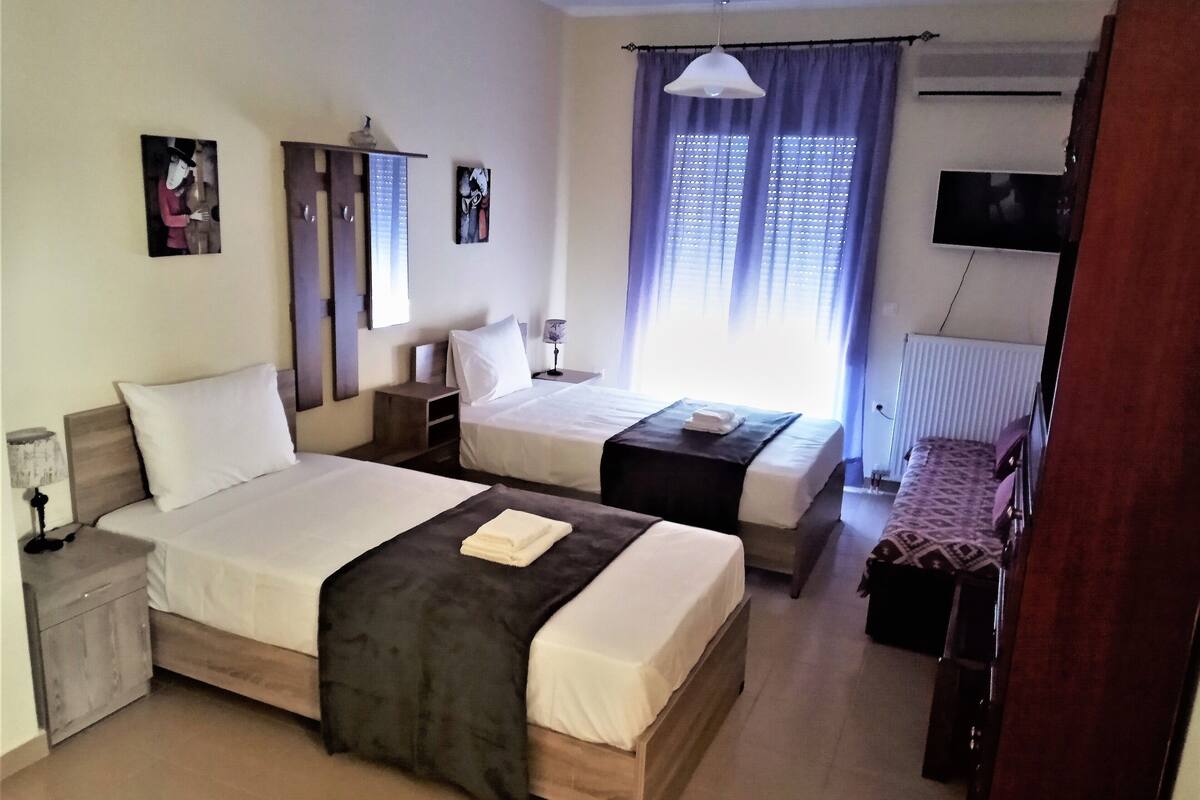 A hotel room with two beds, a desk, a chair, a TV, and a window with curtains.