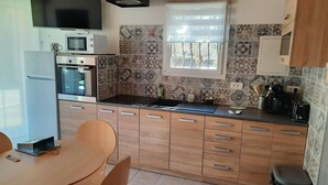 Cozinha compacta com micro-ondas, forno e pia. Há uma janela com persianas, e as paredes são revestidas com padrões geométricos.