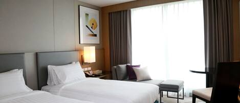 Habitación de hotel con dos camas grandes, un escritorio, una silla y un ventanal con cortinas.