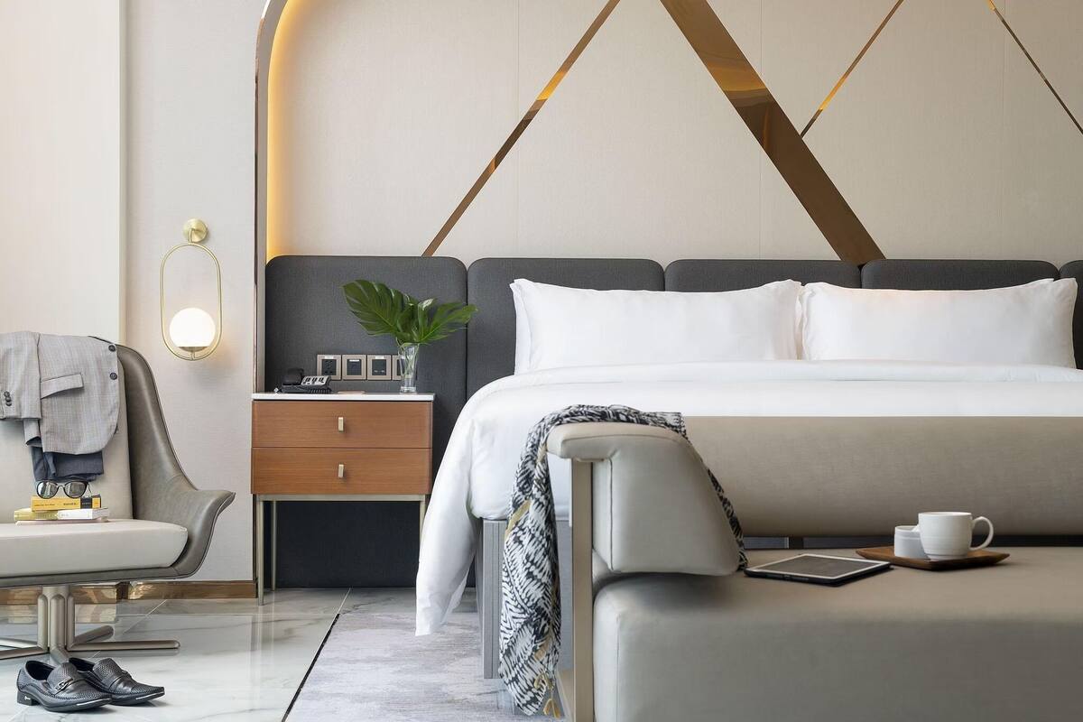 A modern hotel room with a large bed, bedside table, and a chair.