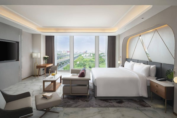 A modern hotel room with a large bed, a desk, a chair, a TV, and a view of the city. - Asawin Grand Convention Hotel (Bangkok)