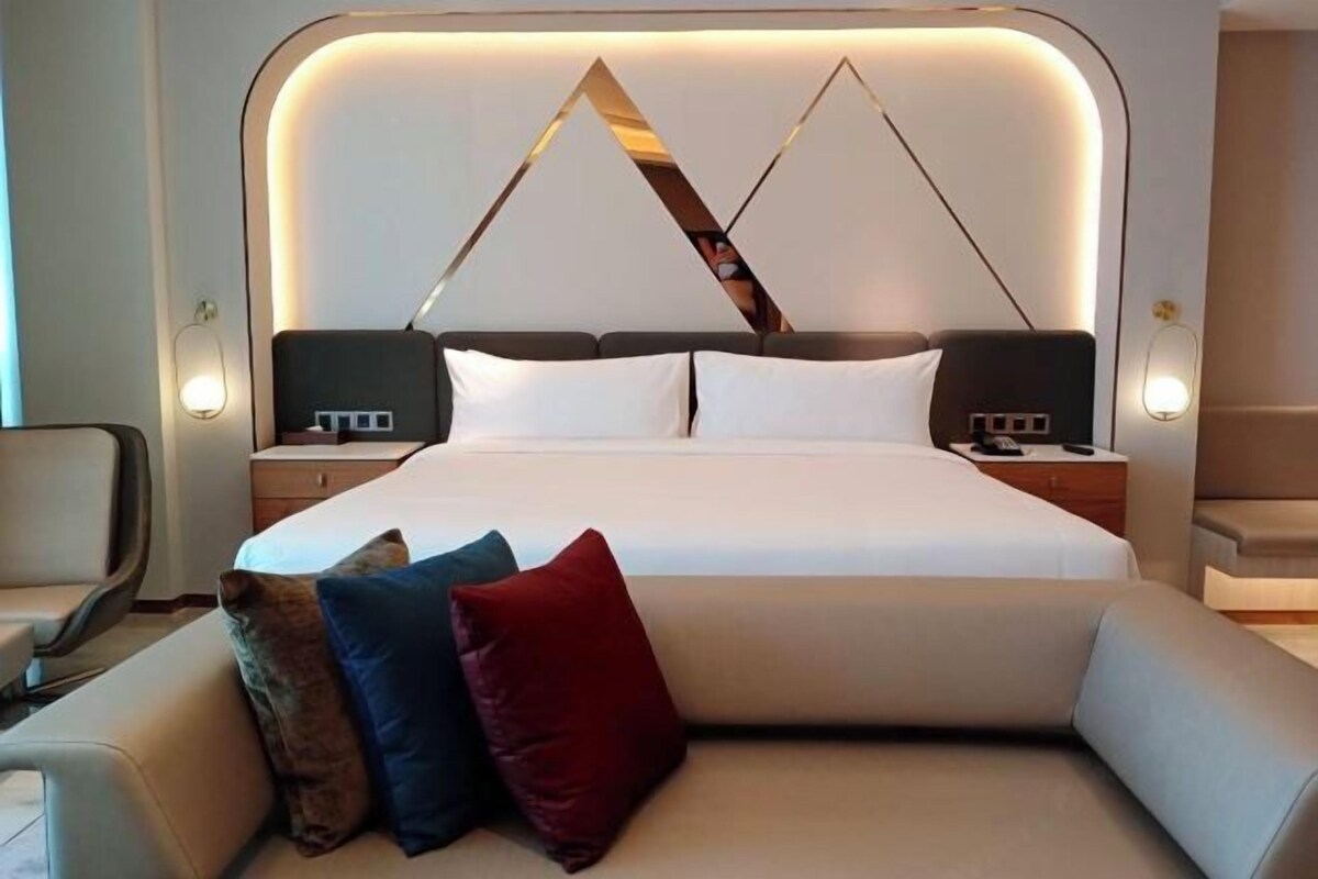 A modern hotel room with a large bed, two bedside tables, and a sofa with cushions.