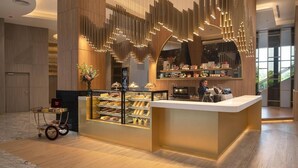 A modern hotel lobby with a central counter, decorative lighting, and a display of pastries. - Asawin Grand Convention Hotel (Bangkok)