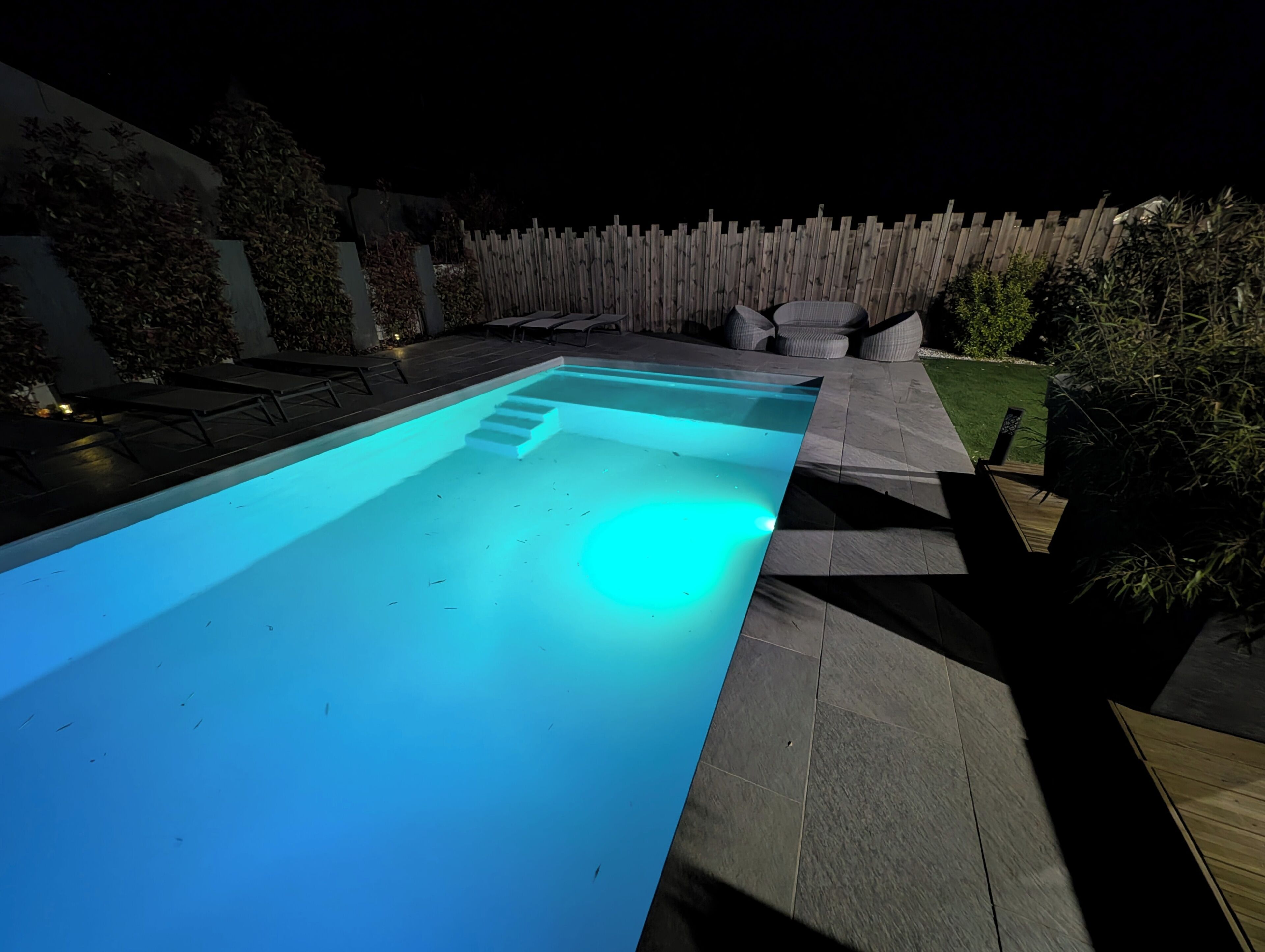 A swimming pool with steps, surrounded by a wooden fence and outdoor furniture.