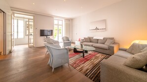 Ein geräumiges Wohnzimmer mit einer Couch, Sesseln, einem Glastisch und einem Flachbildfernseher.