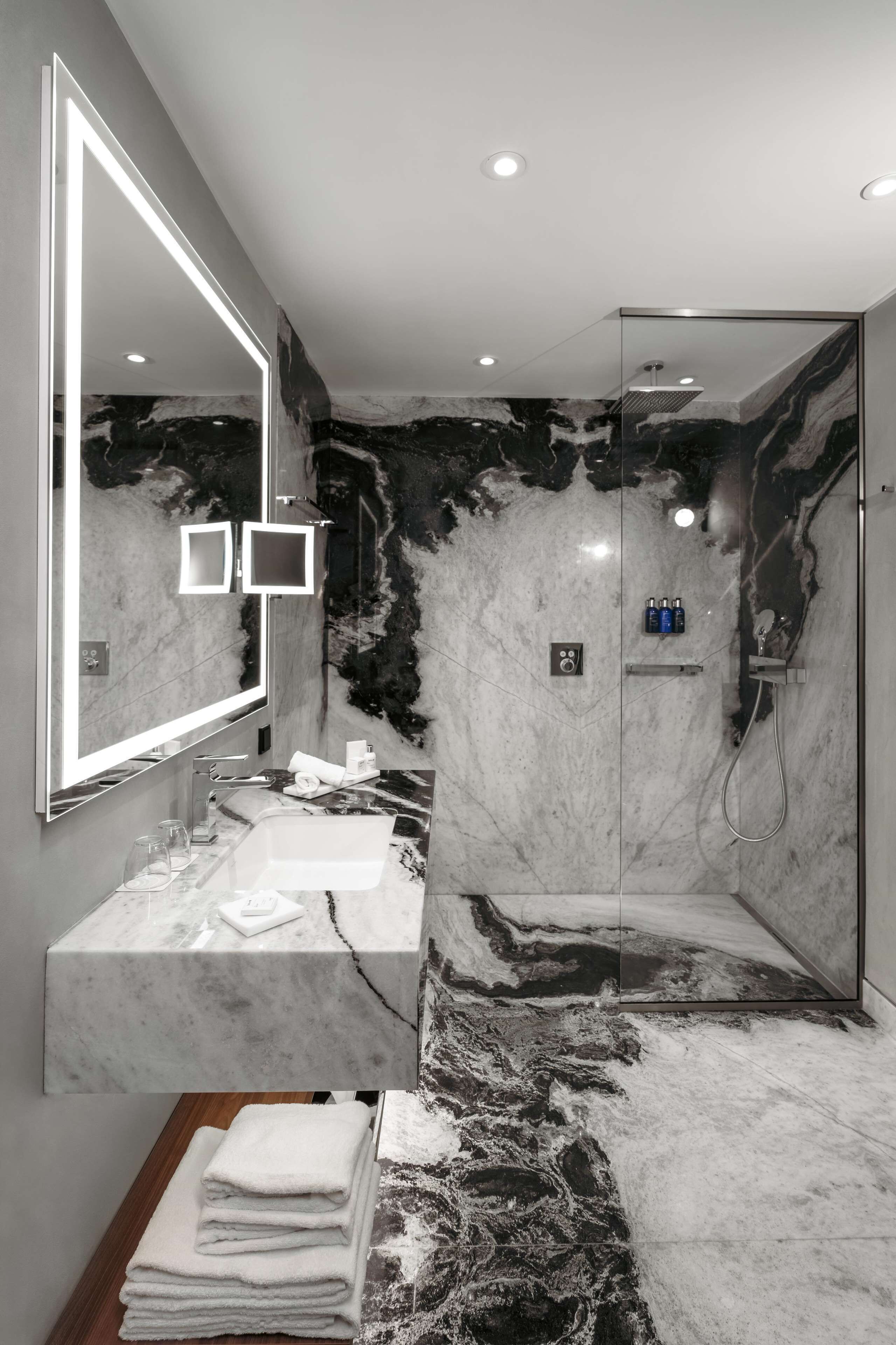 A modern bathroom with a marble vanity, a large mirror, and a glass-enclosed shower.