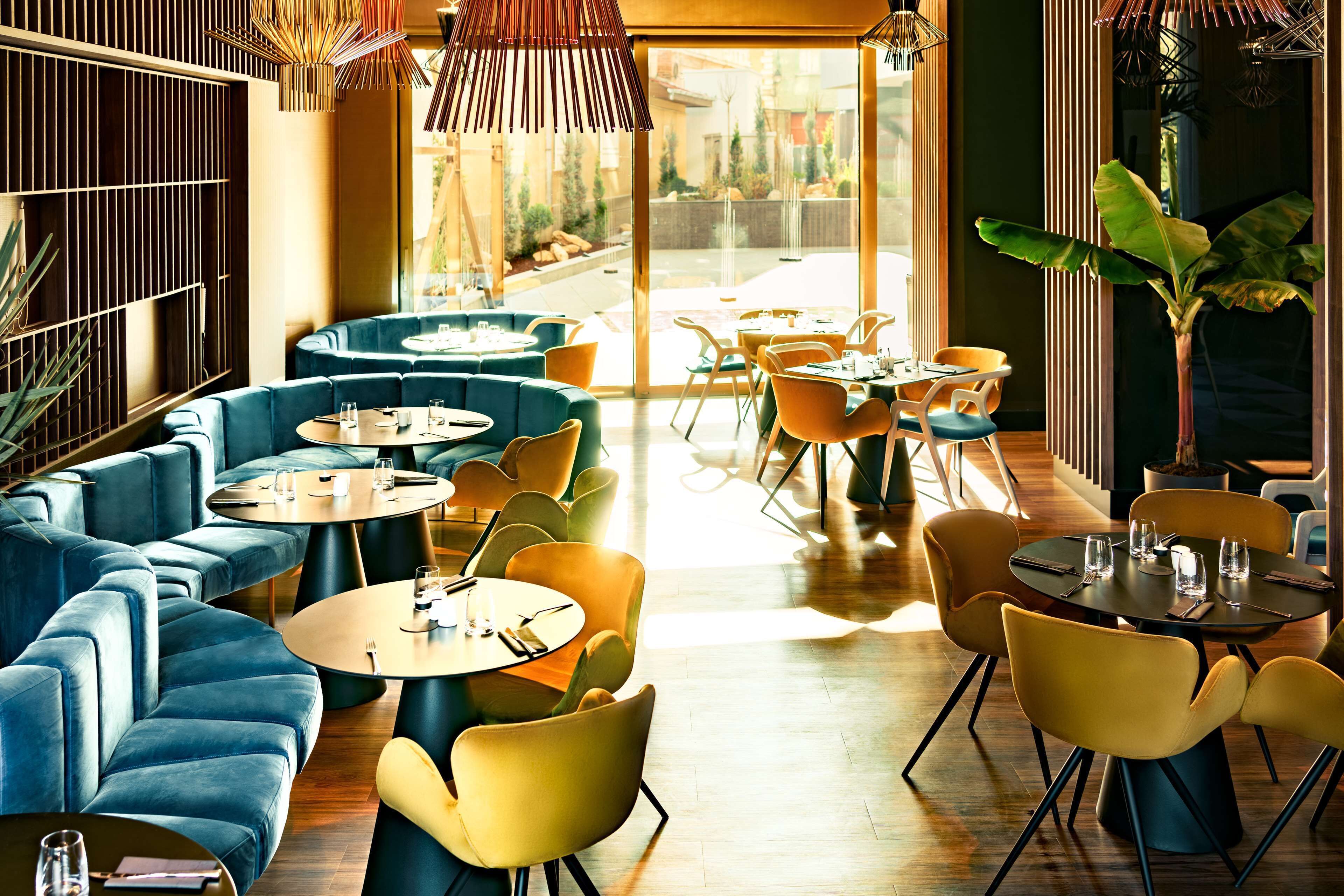 Un restaurante moderno con asientos azules y amarillos, ventanas amplias y suelo de madera.
