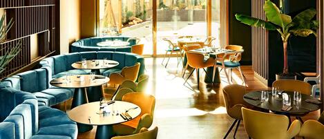 A modern restaurant with blue and yellow seating, large windows, and a wooden floor.
