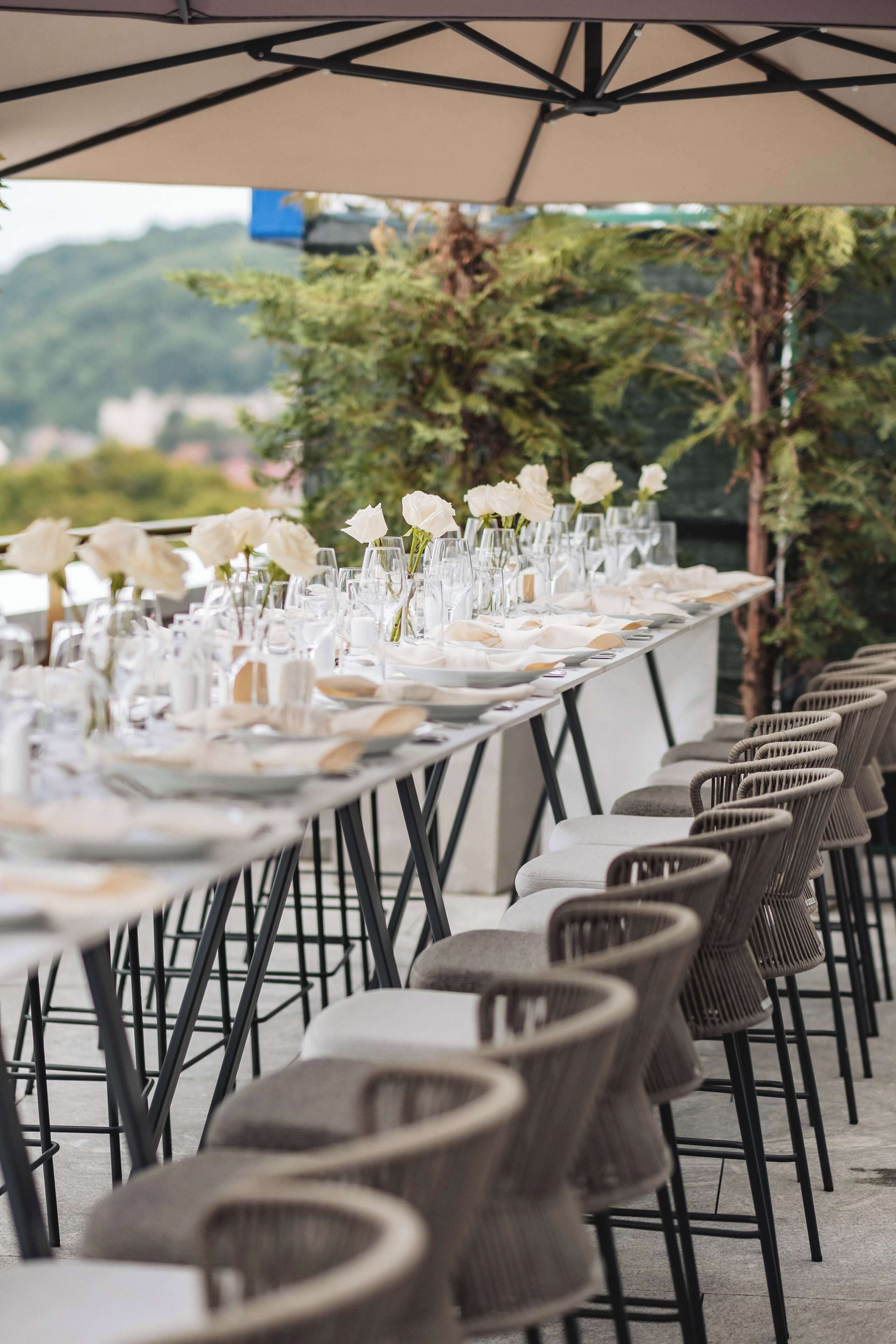 Una larga mesa de comedor adornada con flores blancas y cristalería, rodeada de sillas de mimbre.