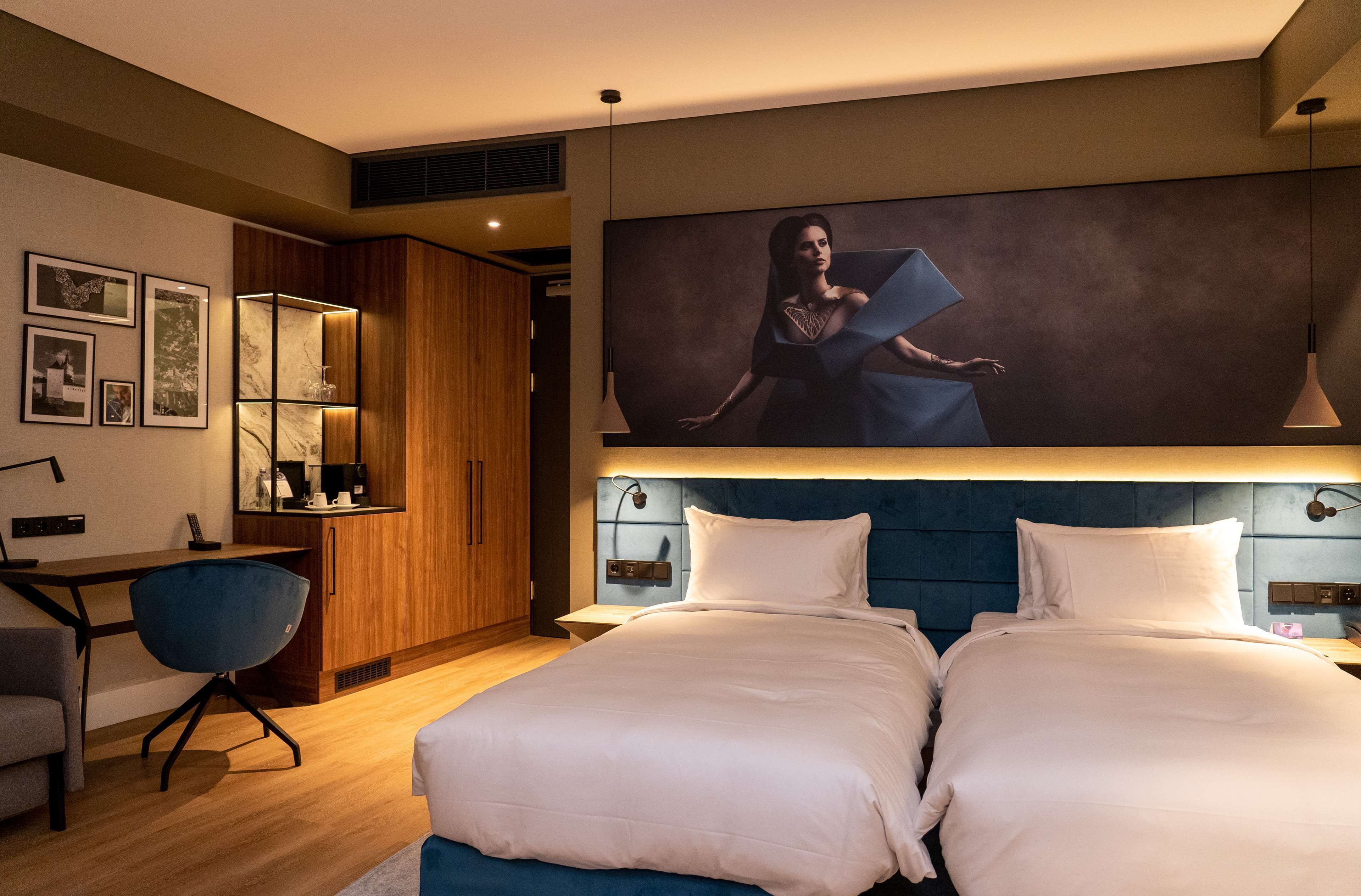 A hotel room with a large bed, a desk, a chair, and a painting on the wall.